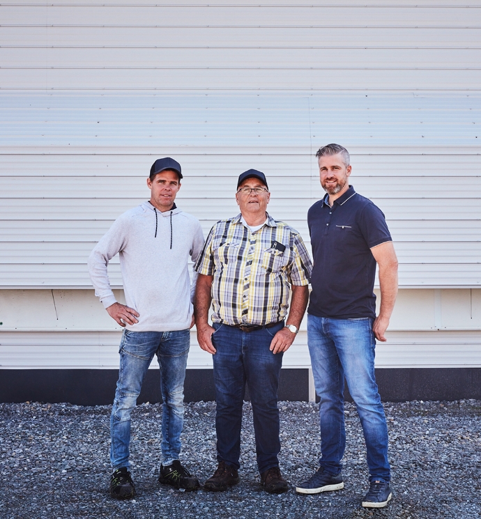 Three smiling farmers standing in front of their barn